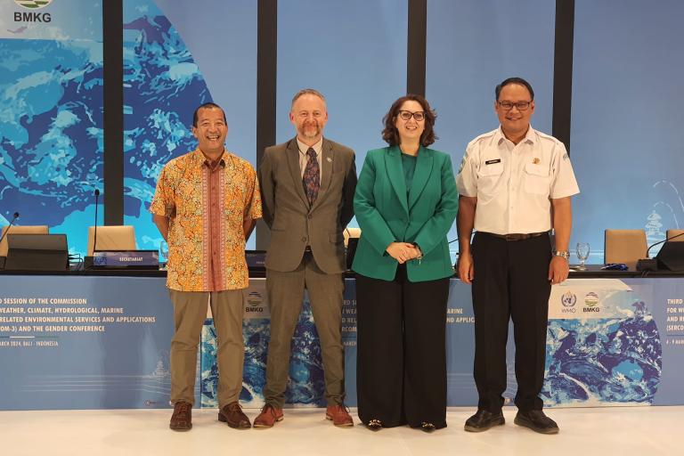 Four people standing in front of a blue background.