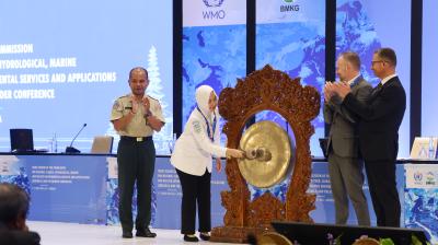 A woman strikes a ceremonial gong, while 3 other people applaud.