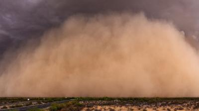 A large dust storm sweeps across a barren, desert landscape with a road on the left side of the image. The sky is dark and ominous.