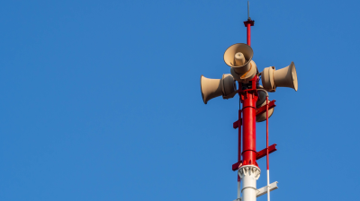 A red and white pole with several loudspeakers mounted on top, against a clear blue sky.