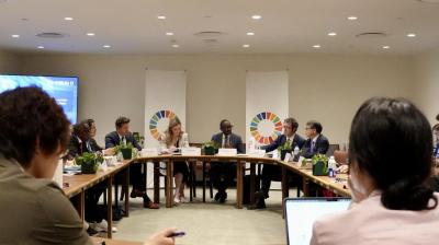 A group of diverse individuals in formal attire sit around a U-shaped table in a conference room.