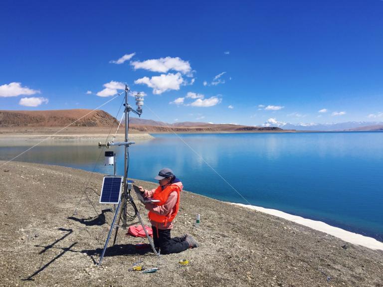 A man is standing next to a lake with a device in front of him.